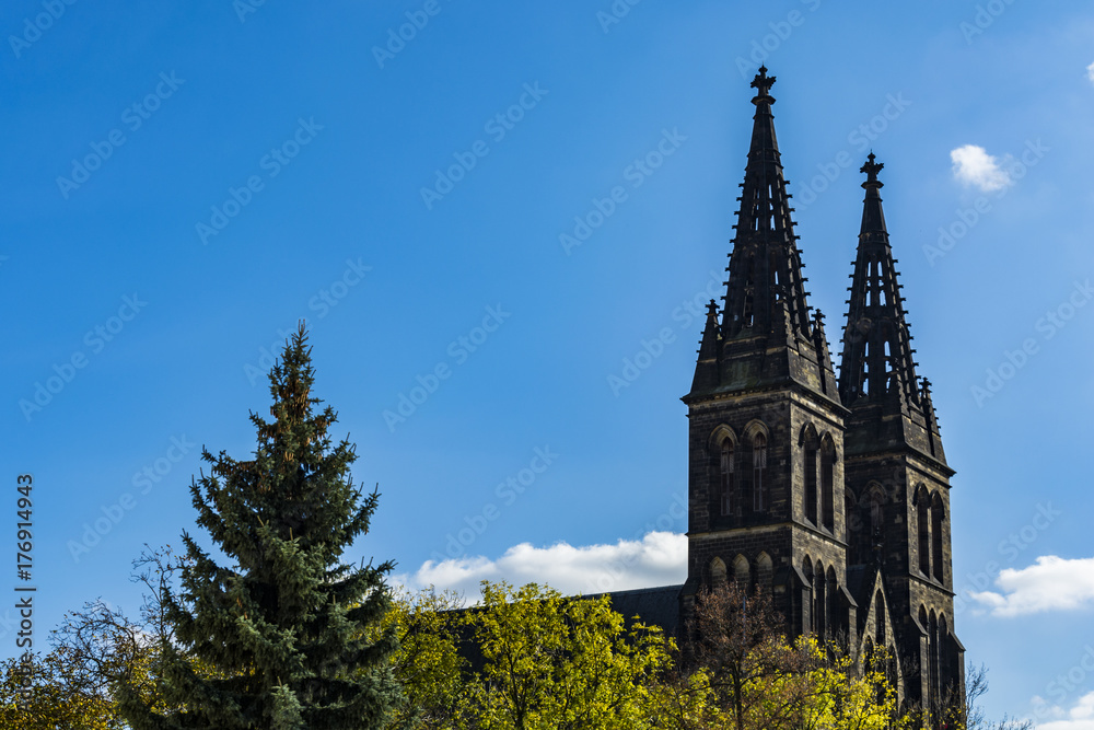 The Vysehrad towers hidden behind trees under clear blue sky. Czech national landmark in Prague.