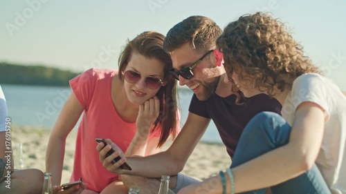Young people having fun on the beach using phones. Medium shot. Soft Focus.