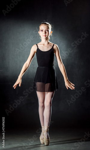 Ballerina. Cute little girl posing and dancing in studio. A little dancer. Dark background. Black dress.