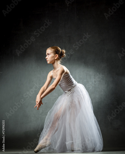 Beautiful young ballerina is dancing in the studio on a dark background. A little dancer. Ballet dancer. © Vadim