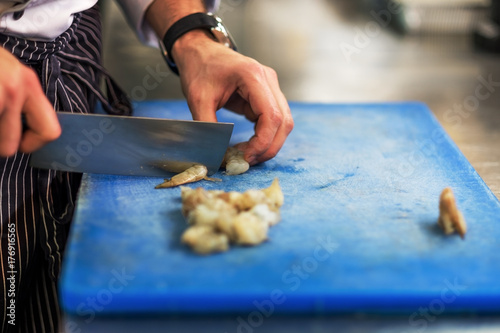 Chef is cutting raw shrimp with big special knife photo