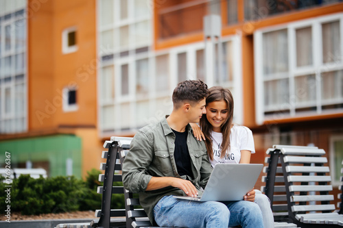 Happy young couple using laptop while sitting on bench in park and smiling each other photo