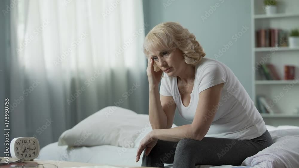 Menopause. Adult female sitting on bed and suffering from migraine, health Menopause. Adult female sitting on bed and suffering from migraine, health