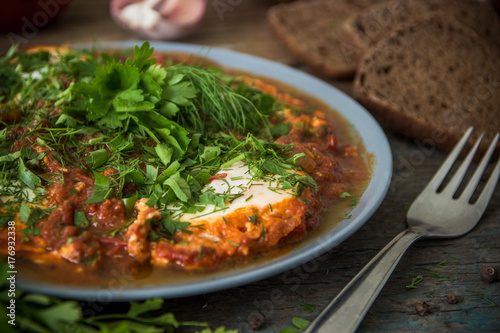 Shakshuka - jewish traditional recipe. Breakfast with fried eggs, tomato sause, pepper and green