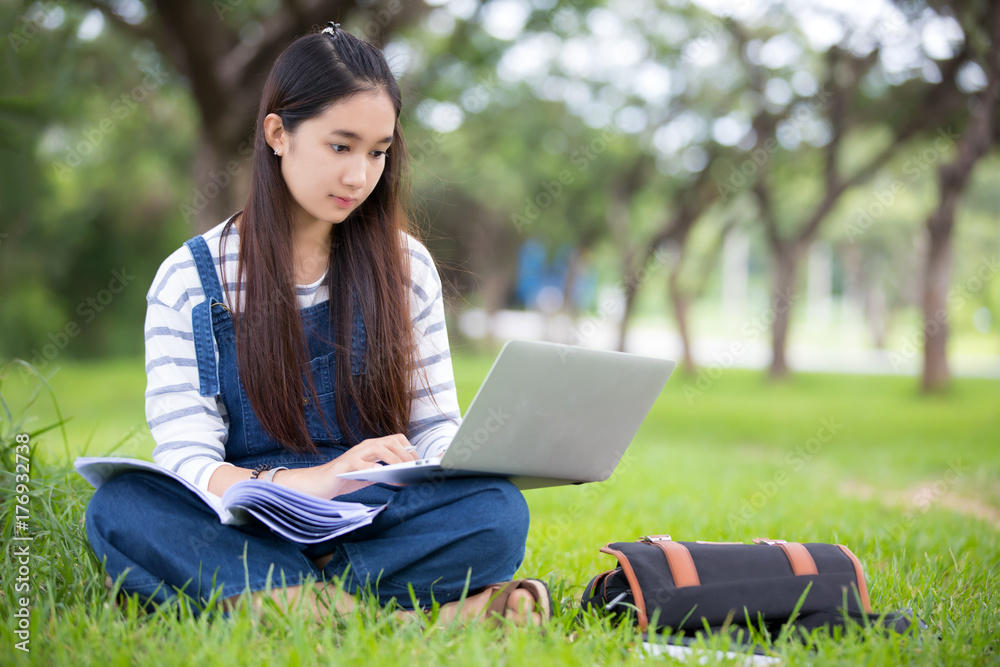 Smiling beautiful Asian girl reading book and working at tree on park in summer for relax time Smiling beautiful Asian girl reading book and working at tree on park in summer for relax time