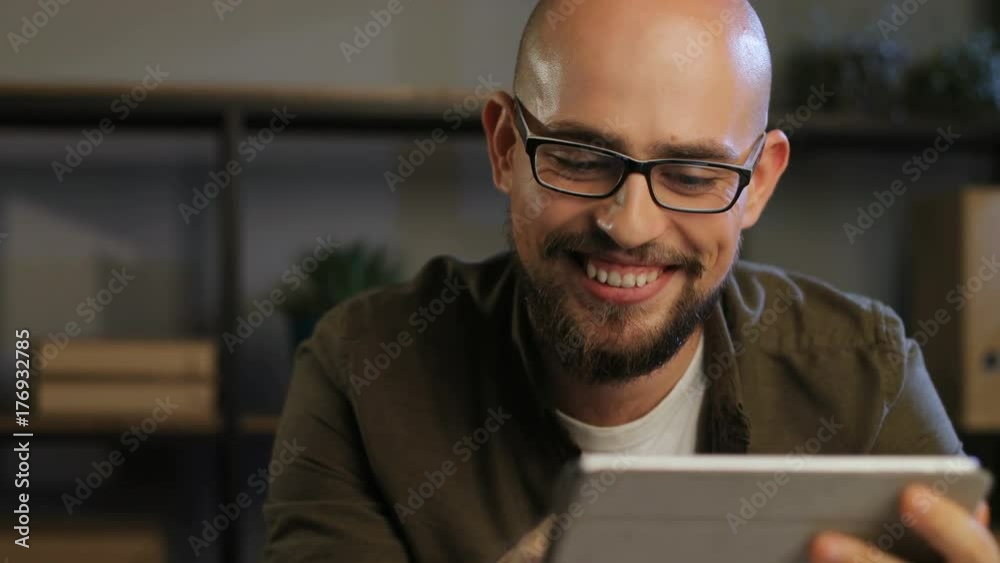 Portrait of handsome smiling man using tablet device for chatting with business partner in the office during evening. Portrait of handsome smiling man using tablet device for chatting with business partner in the office during evening.