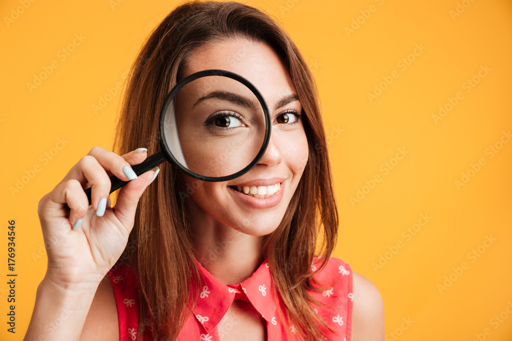 Close up of young cheerful brunette woman looking through magnifying glass Close up of young cheerful brunette woman looking through magnifying glass