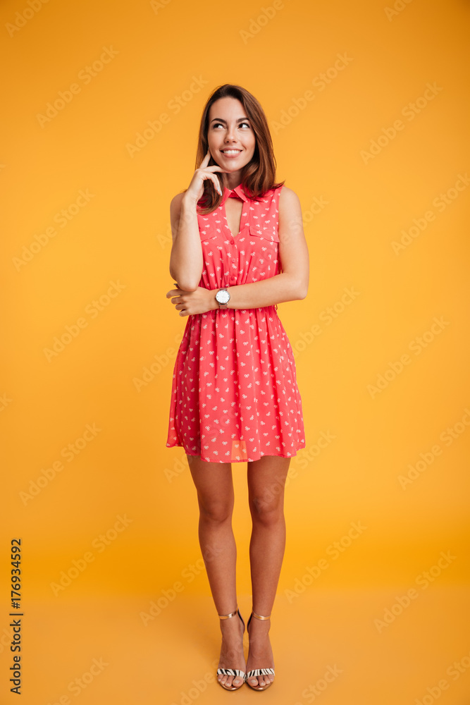 Full length portrait of beautiful girl in red dress touching her chin, looking upward Full length portrait of beautiful girl in red dress touching her chin, looking upward