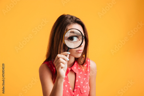 Close up of young serious brunette woman looking through magnifying glass