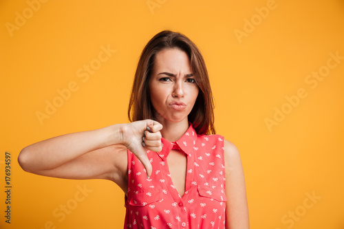 Young upset brunette woman showing thumb down gesture, looking at camera photo