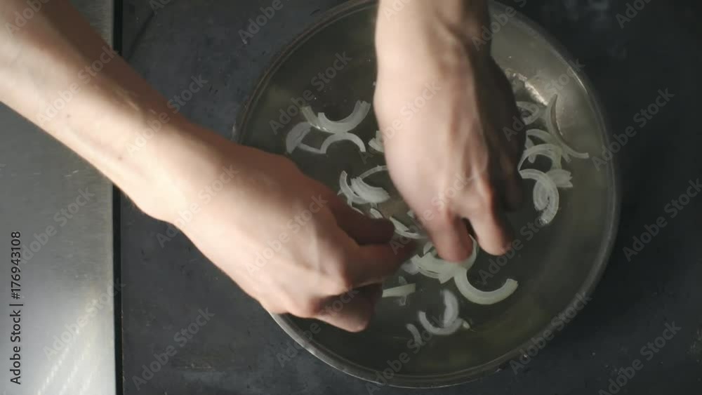 Top view of hands of male cook putting chopped onions on hot pan to fry in sizzling oil Top view of hands of male cook putting chopped onions on hot pan to fry in sizzling oil