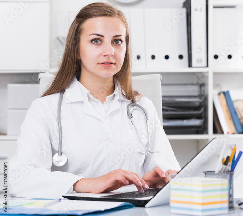 Doctor in uniform is working behind laptop