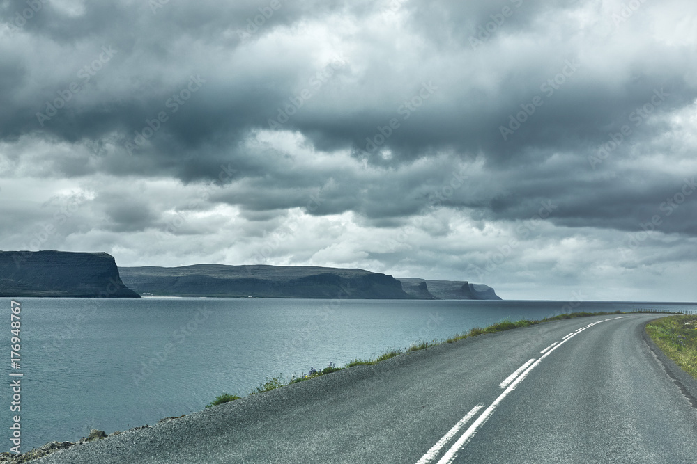 Travel to Iceland. plot of asphalt road in a dark cloudy mountain landscape. focus on the road Travel to Iceland. plot of asphalt road in a dark cloudy mountain landscape. focus on the road