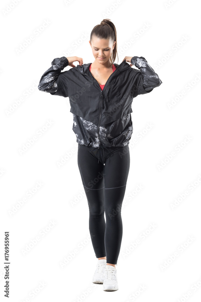 Smiling looking down sporty woman adjusting tracksuit jacket hoodie prepare for training. Full body length portrait isolated on white background.