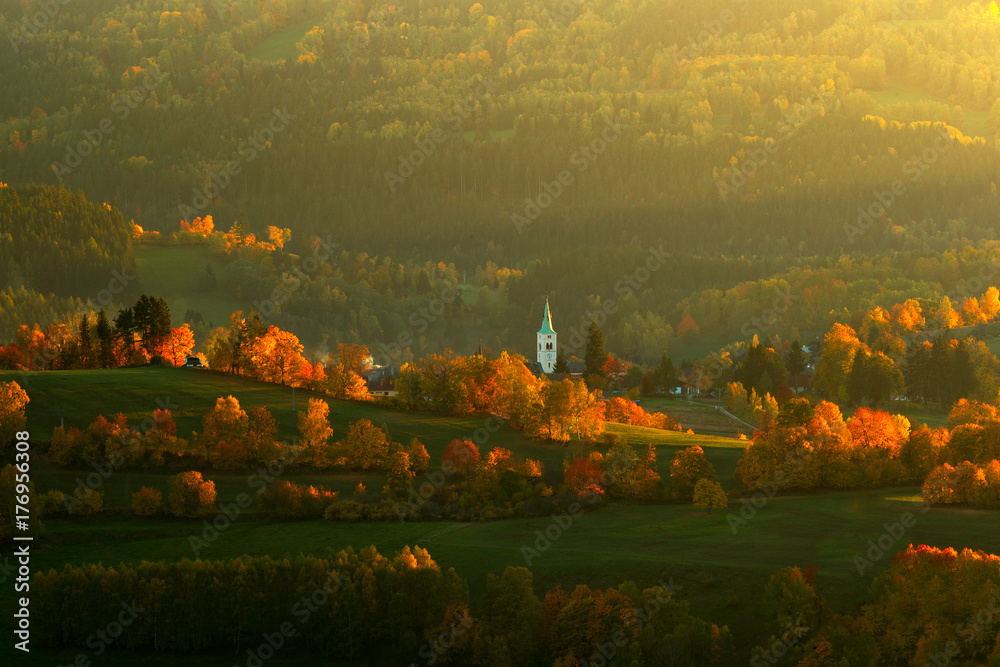 Evening in Kasperske hory church, Sumava, Czech Republic. Cold day in Sumava National park, hills and villages in orange trees, misty view on czech landscape, autumn scene. Evening landscape with sun.