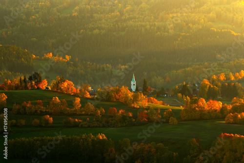 Evening in Kasperske hory church  Sumava  Czech Republic. Cold day in Sumava National park  hills and villages in orange trees  misty view on czech landscape  autumn scene. Evening landscape with sun.