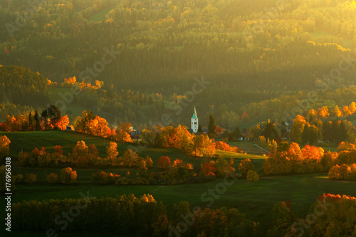 Evening in Kasperske hory church, Sumava, Czech Republic. Cold day in Sumava National park, hills and villages in orange trees, misty view on czech landscape, autumn scene. Evening landscape with sun. photo