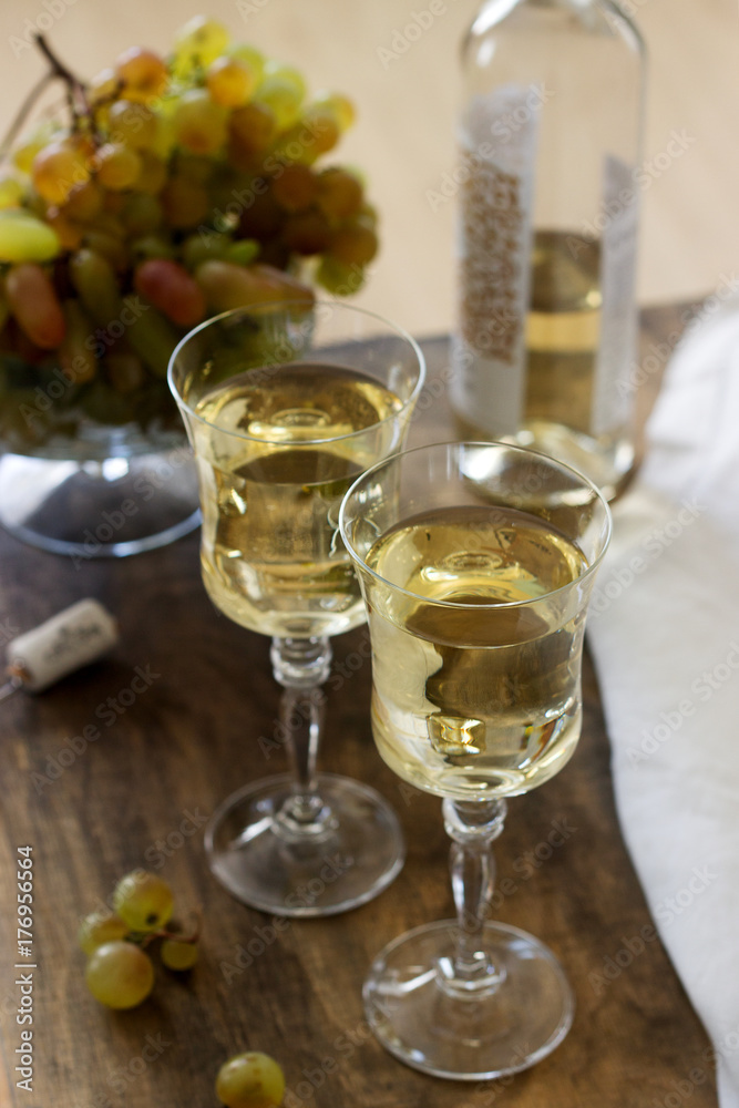 White wine with glass goblets and grape bunches on a wooden background.
