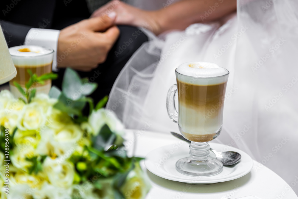 Hands of the bride and groom for a cup of coffee. Wedding bouquet on the table. Hands of the bride and groom for a cup of coffee. Wedding bouquet on the table.