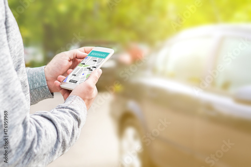 Online ride sharing and carpool mobile application. Rideshare taxi app on smartphone screen. Modern people and commuter transportation service. Man holding phone with a car in background. photo