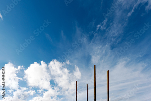 Fototapeta Four poles appear to be soaring into a bright blue cloudy sky