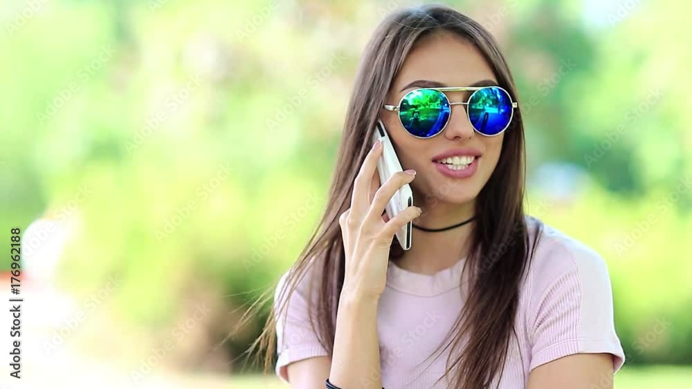 Happy woman in glasses with long hair speaks on smartphone. Girl speaks on cell phone. Female with white smartphone. Beautiful woman in glasses talks on the mobile phone Happy woman in glasses with long hair speaks on smartphone. Girl speaks on cell phone. Female with white smartphone. Beautiful woman in glasses talks on the mobile phone