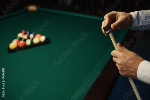 Caucasian Man wipes a cue with chalk ready to start game.