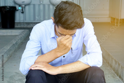 Depressed man holding the forehead with his hand sitting on the ladder of the toilet