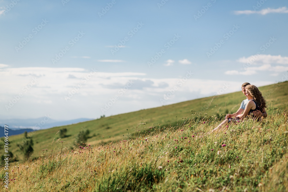 Mand and woman sit hugging on the grass before beautiful landscape