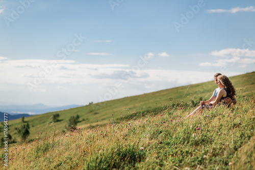 Mand and woman sit hugging on the grass before beautiful landscape