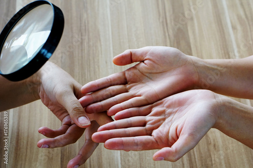 Fortune teller using magnifying glass to woman's hand to predict the fortune