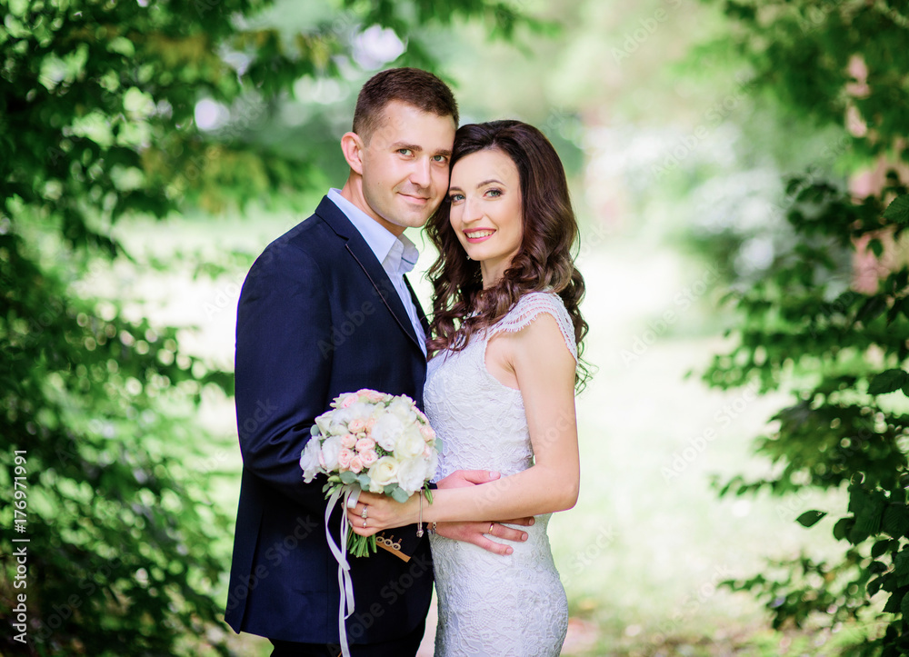 Happy hugging wedding couple stands before green trees