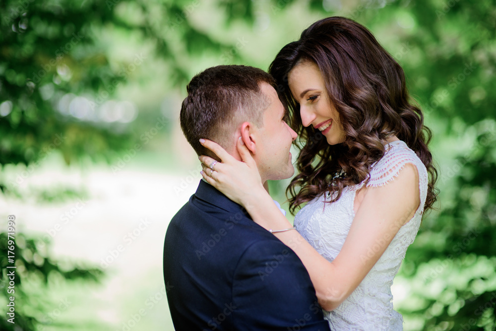 Happy hugging wedding couple stands before green trees