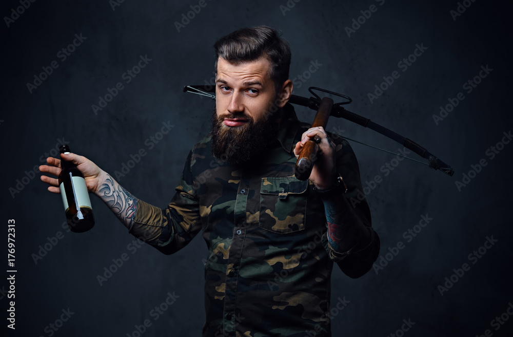 Fototapeta premium A man holds the craft beer bottle and a crossbow.