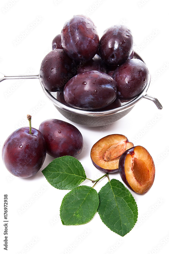 Steel colander with ripe plums, whole and half ripe plums with leaf isolated on a white background.. Steel colander with ripe plums, whole and half ripe plums with leaf isolated on a white background..