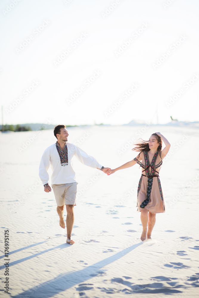 Barefooted couple in bright embroidered clothing runs on a white sand