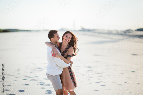 Barefooted couple in bright embroidered clothing hugs tender on a white sand © IVASHstudio