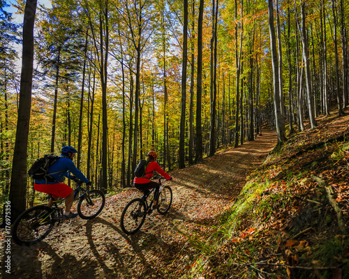 Cycling, mountain biker couple on cycle trail in autumn forest. Mountain biking in autumn landscape forest. Man and woman cycling MTB flow uphill trail.