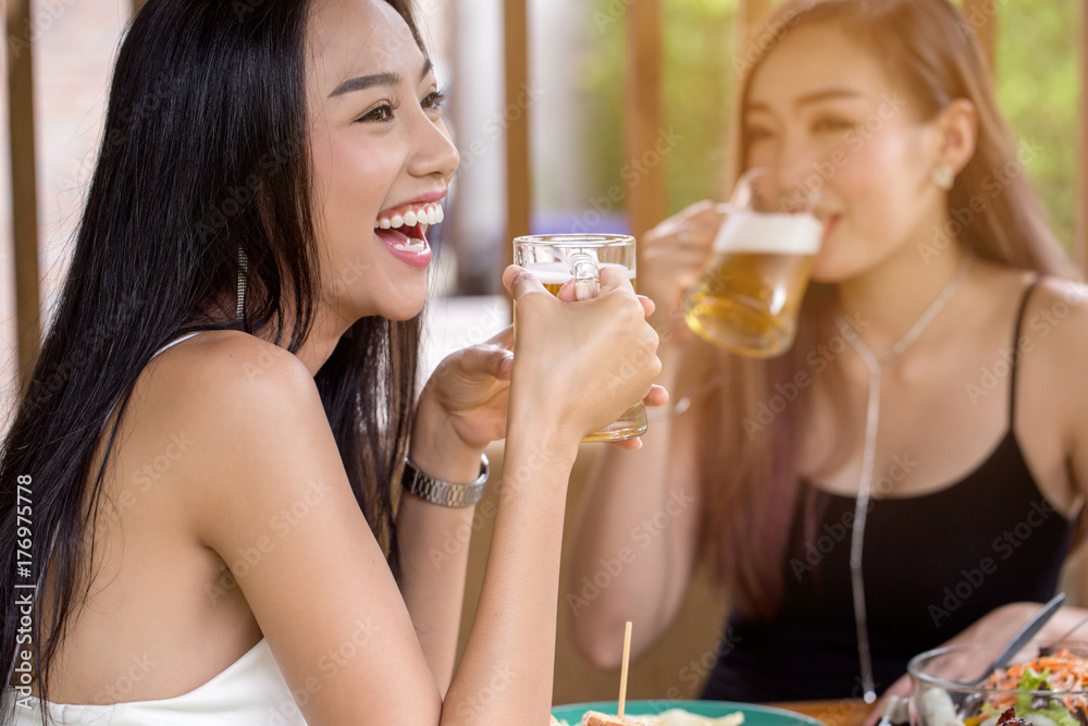 Beautiful Asian women are holding a glass of beer and cheers with her friends. She have smiling face and laughter. Beautiful Asian women are holding a glass of beer and cheers with her friends. She have smiling face and laughter.