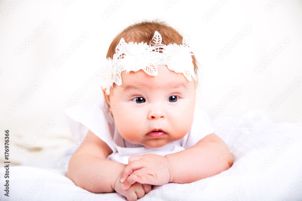 cute kid lying on the white background. Portrait of baby in white gown and bandage on her head on a white background cute kid lying on the white background. Portrait of baby in white gown and bandage on her head on a white background