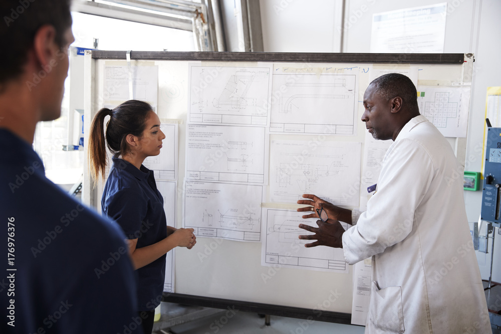 Engineer instructs two apprentices at white board, close up Engineer instructs two apprentices at white board, close up