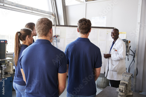 Engineer instructing apprentices at white board, back view