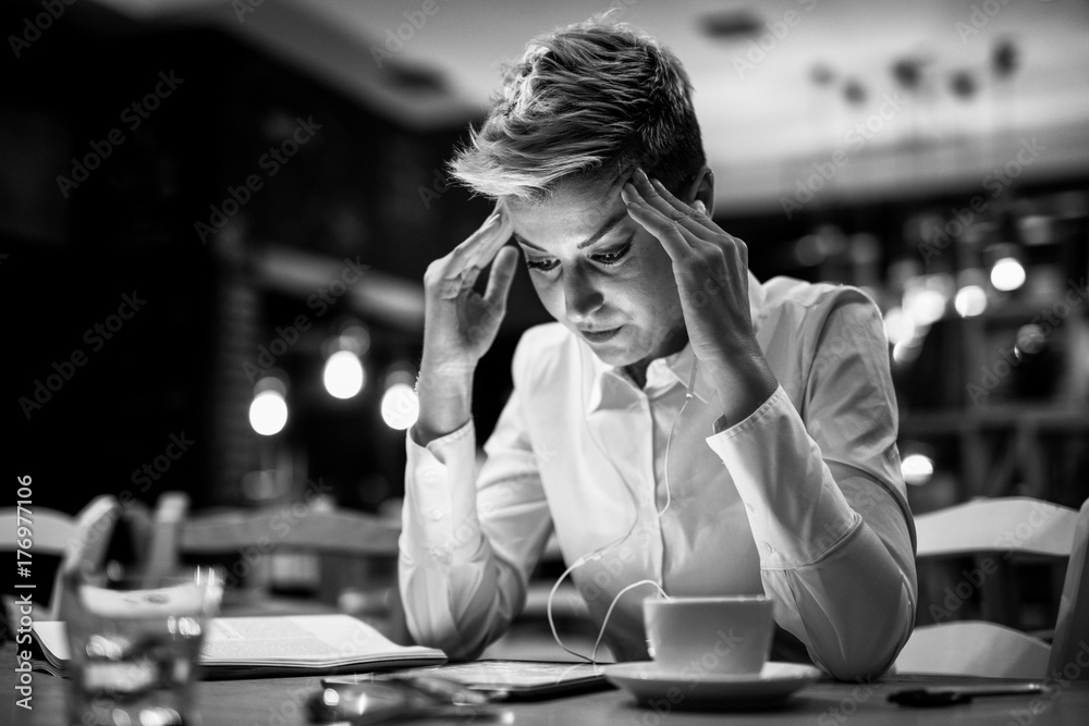 Obraz premium Stressed young woman entrepreneur sitting at the table with business plans and a cup of coffee.Black and white.