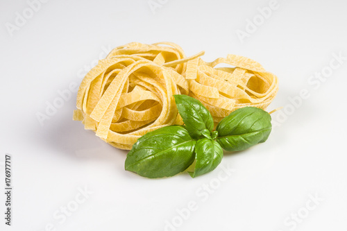 Uncooked and raw tagliatelle with basil leaves isolated on white.