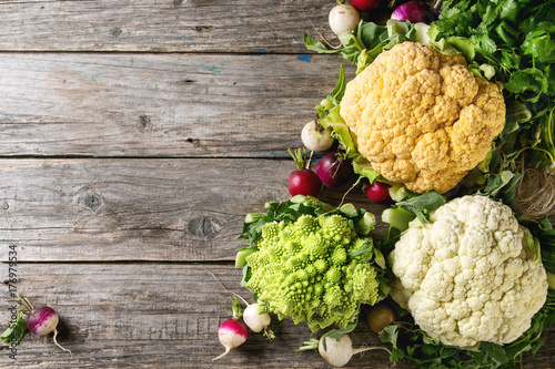 Variety of fresh raw organic colorful cauliflower, cabbage romanesco and radish with bundle of coriander over old wooden background. Top view with copy space. Food farm market concept