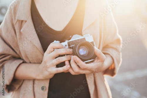 Closeup of woman in hipster outfit, holding vintage analog film camera, zooming and focusing in warm soft evening sunlight
