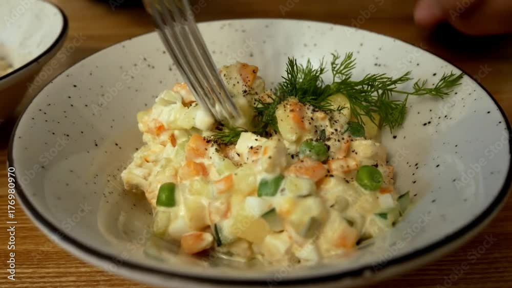 Female hand Peppers Olivier salad and dials it with a fork on a wooden table in a restaurant Female hand Peppers Olivier salad and dials it with a fork on a wooden table in a restaurant