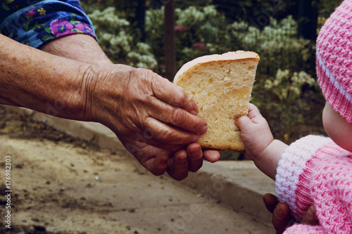 An old grandmother gives a piece of bread to a small child photo