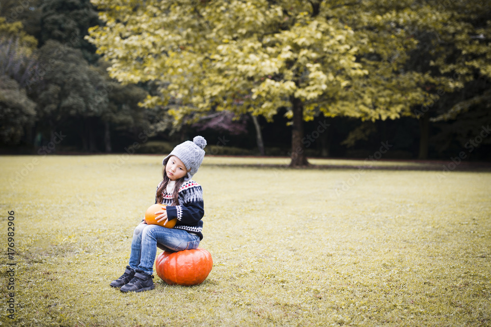 Fototapeta premium Little girl sitting on the pumpkin