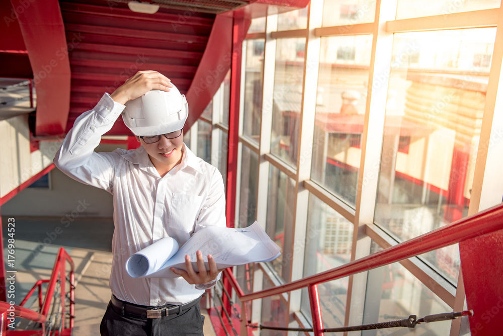 Engineer or Architect checking architectural drawing while wearing a personal protective equipment safety helmet at construction site. Engineering, Architecture and building construction concepts